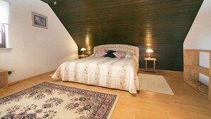 A bedroom with a sloped ceiling, a bed with a patterned bedspread, two bedside lamps, a wooden bench, and a rug.