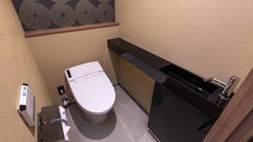 A compact bathroom with a toilet, a sink, and a paper towel dispenser.