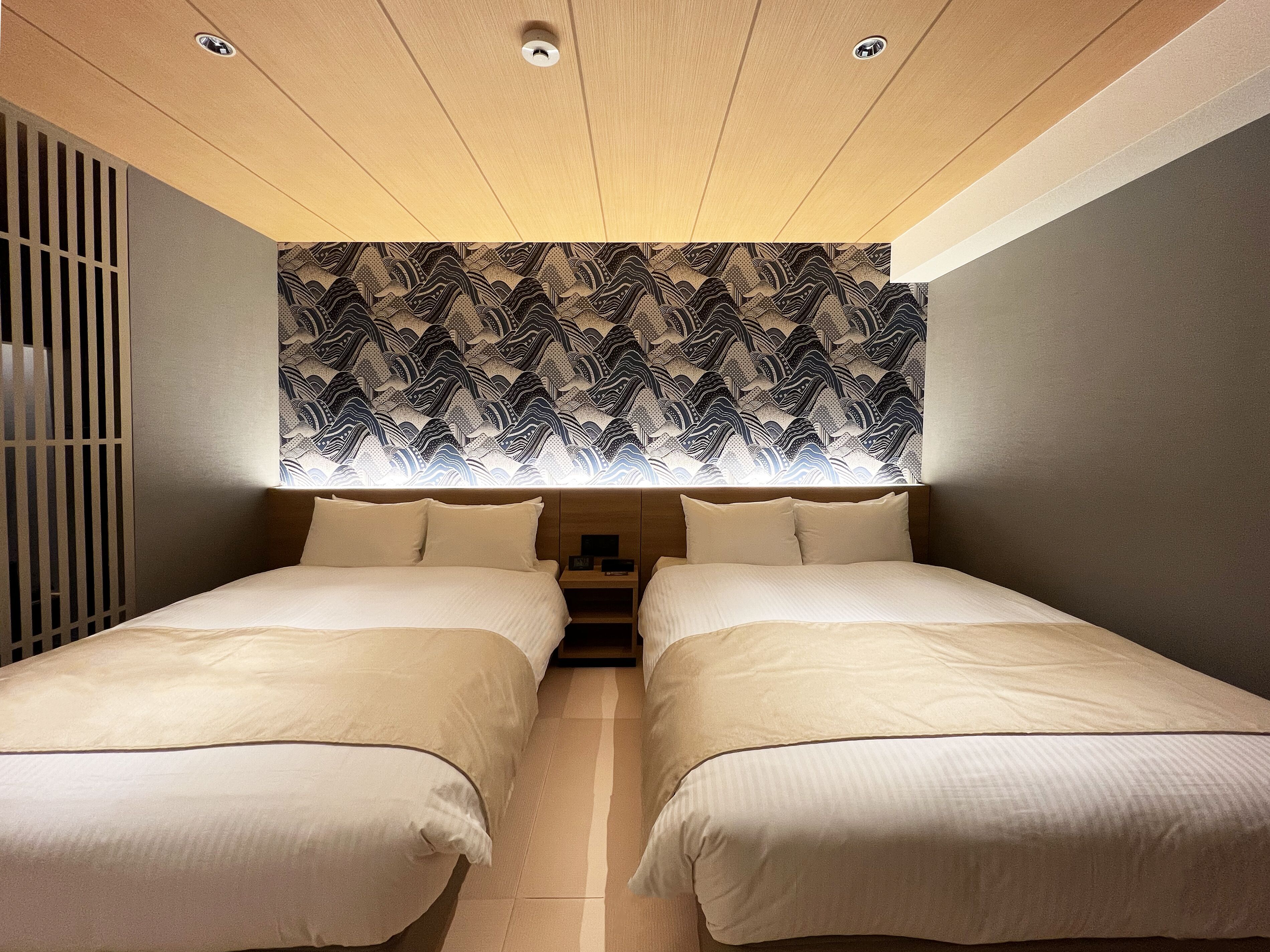 A room with two beds, a patterned headboard, and a ceiling with recessed lighting.