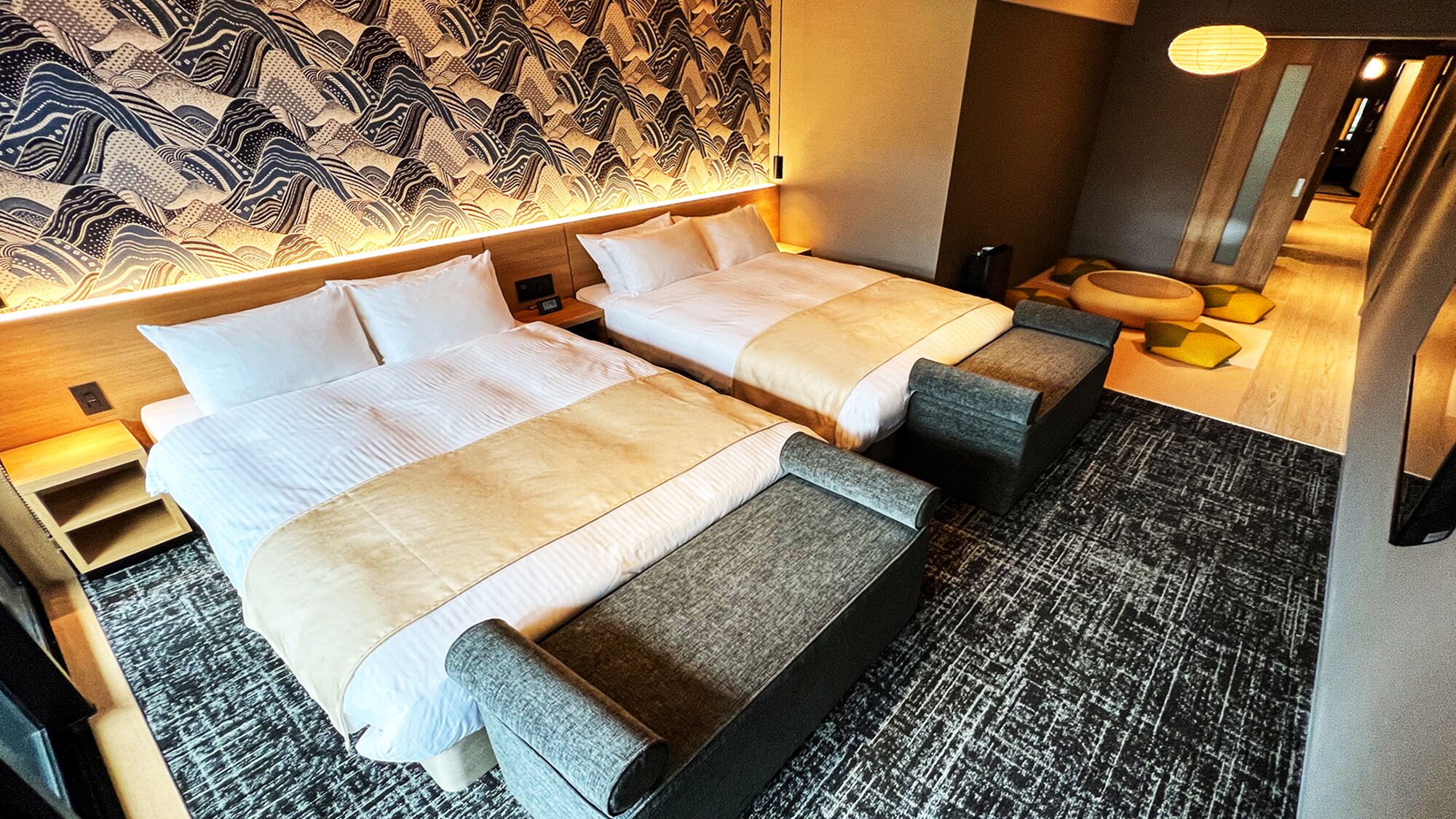 A hotel room with two beds, a patterned headboard, a small seating area, and a mirror.
