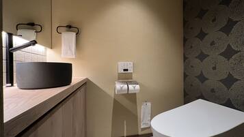 A modern bathroom with a wooden vanity, a black basin, a towel rack, a toilet paper holder, and patterned wallpaper.