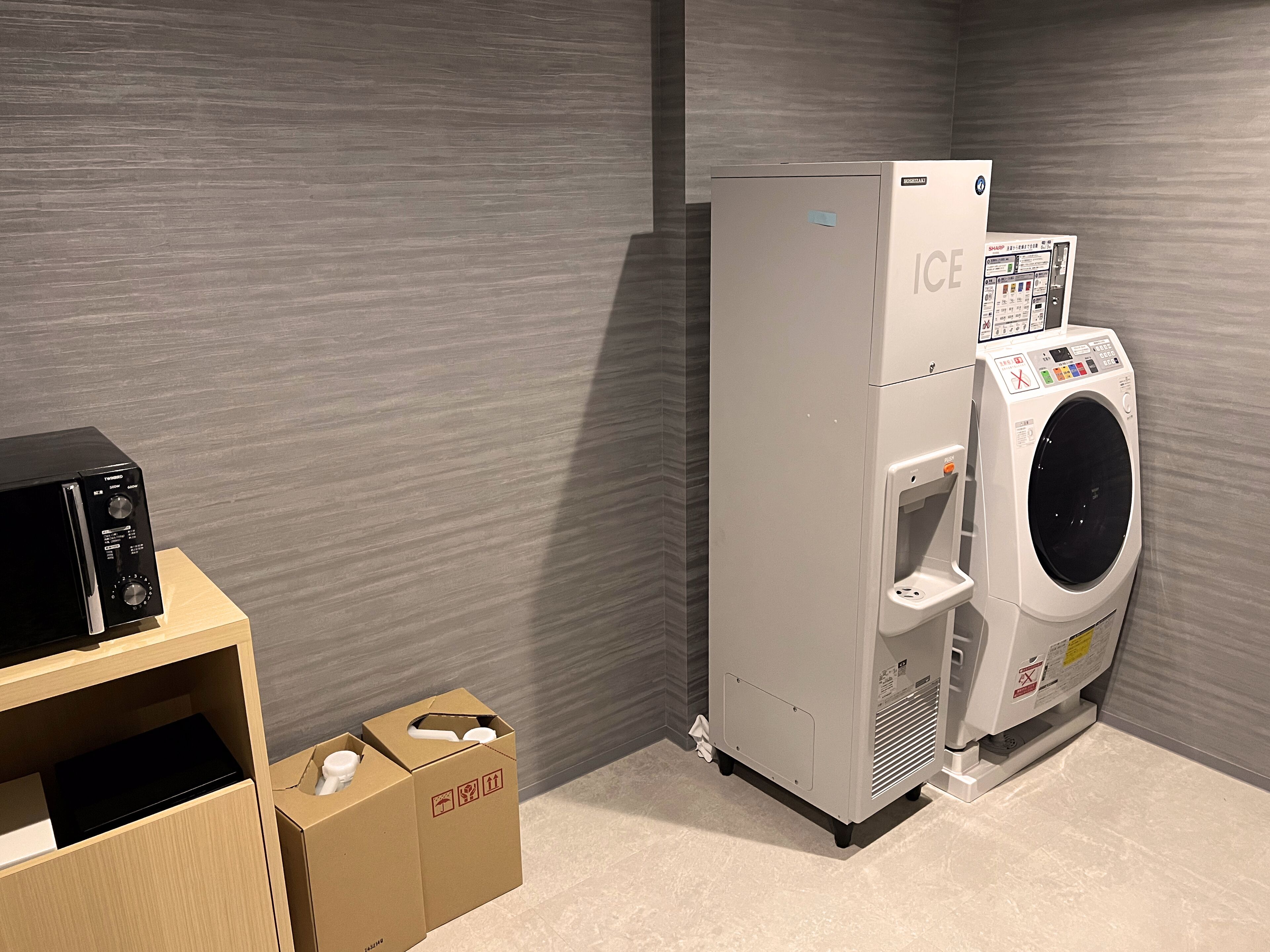 A compact laundry room with a washing machine and a microwave. There are cardboard boxes on the floor.