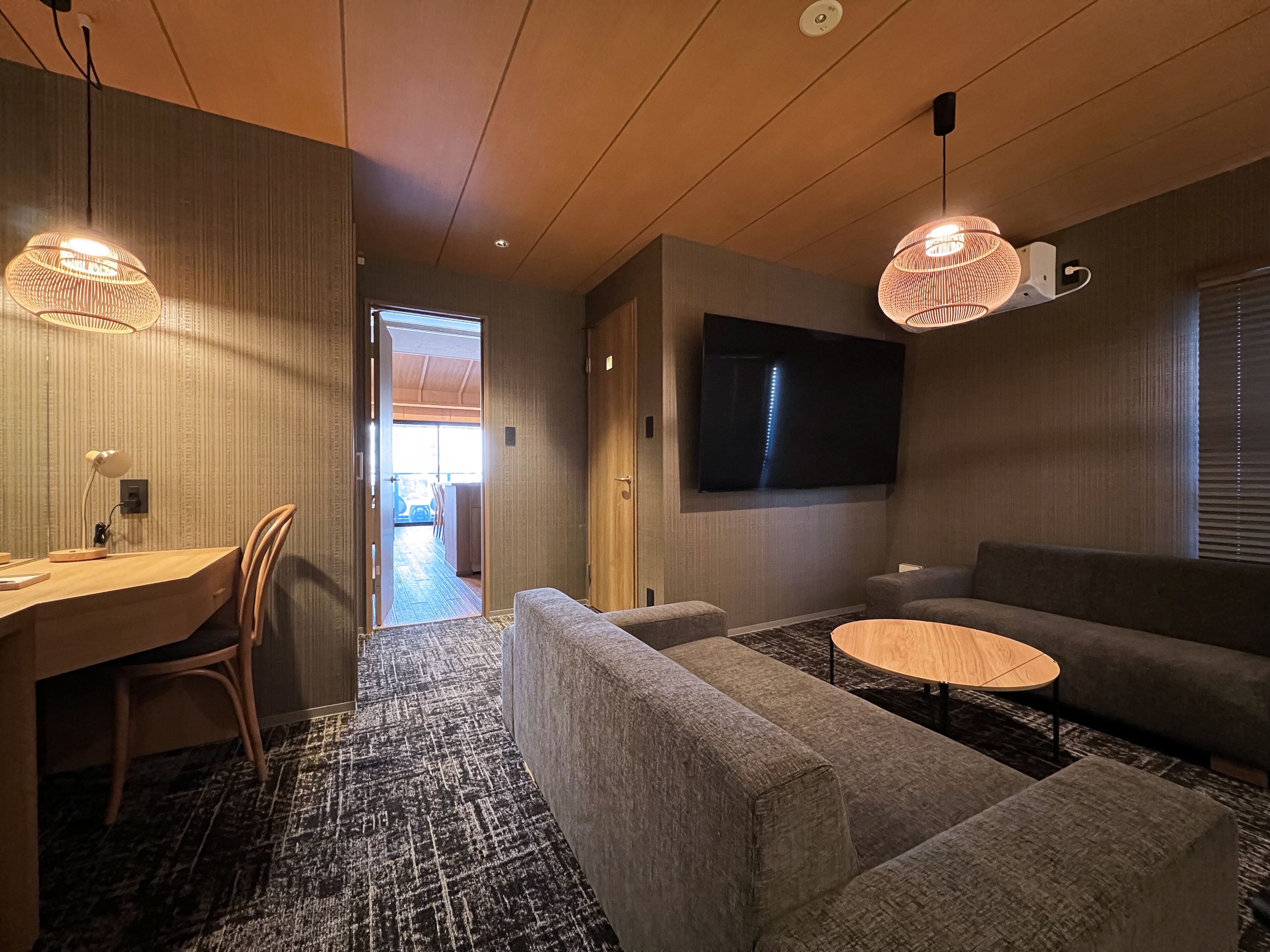 A modern living room with a sofa, a coffee table, a TV mounted on the wall, and a desk with a chair.