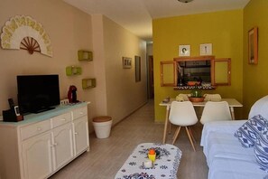 A living room with a TV, a small table with a teapot, and a dining area with chairs and a table. - Belvilla by OYO Apartamento Natura (Andalucía)