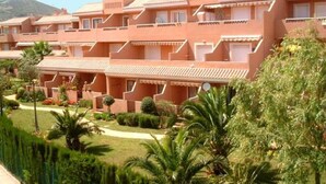 A multi-story hotel with balconies, a well-maintained garden, and a mountainous backdrop.