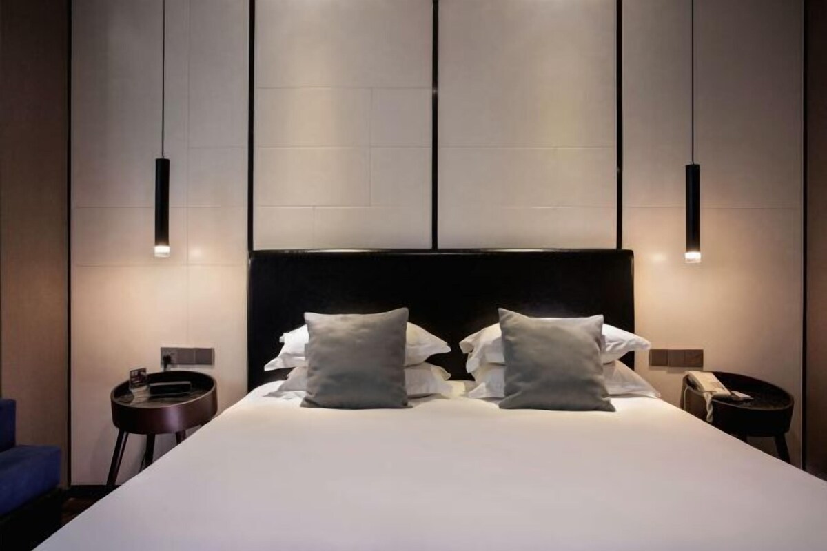 A modern hotel room with a large bed, two bedside tables, and pendant lighting.