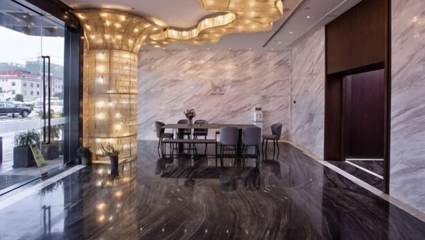 A modern hotel lobby with a marble floor, a dining area with a table and chairs, and a unique ceiling light fixture. - Puyuan X Hotel (Tongxiang)