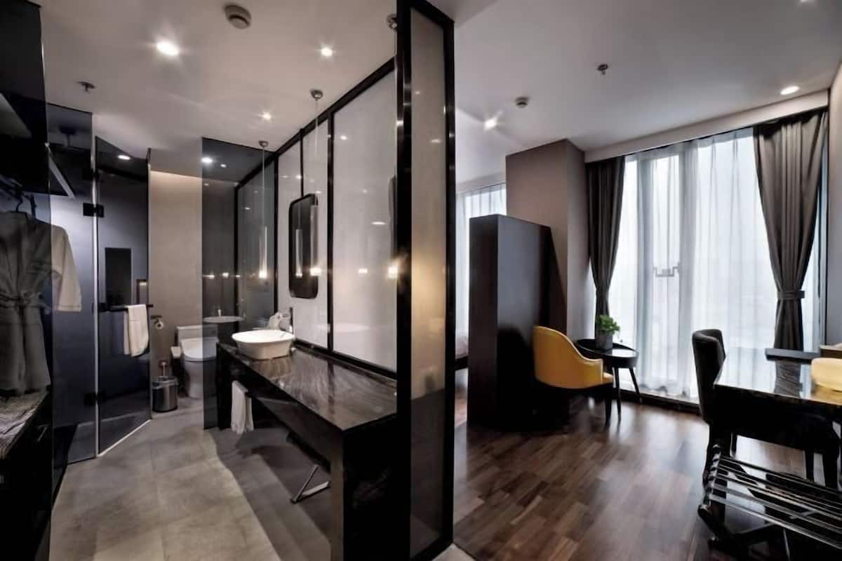 A modern hotel room with a large mirror, a vanity with a sink, a dining area with a table and chairs, and a large window with curtains.