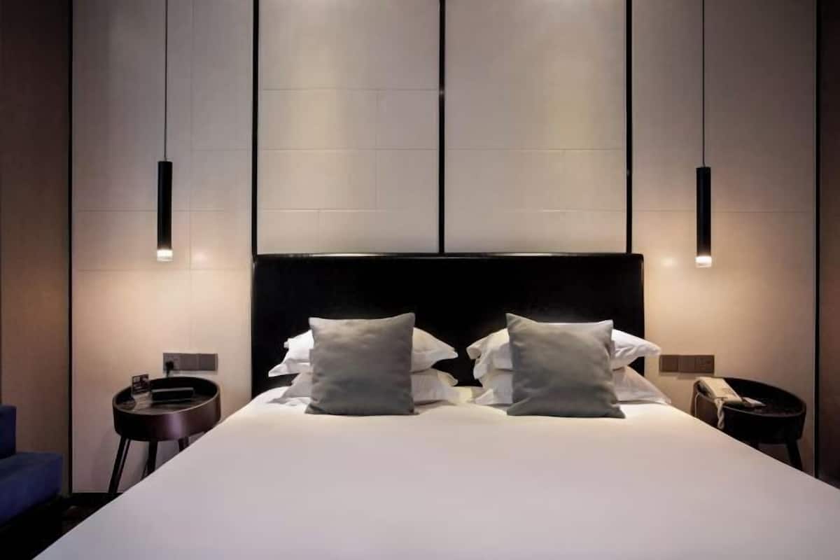 A modern hotel room with a large bed, two bedside tables, and pendant lighting.