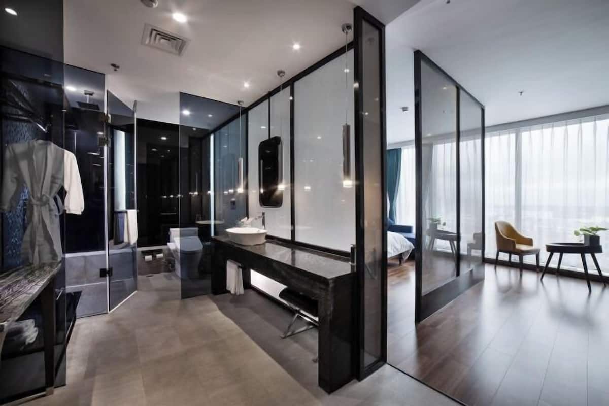 A modern hotel room with a large mirror, a vanity with a sink, a bench, and a view of the city through large windows.