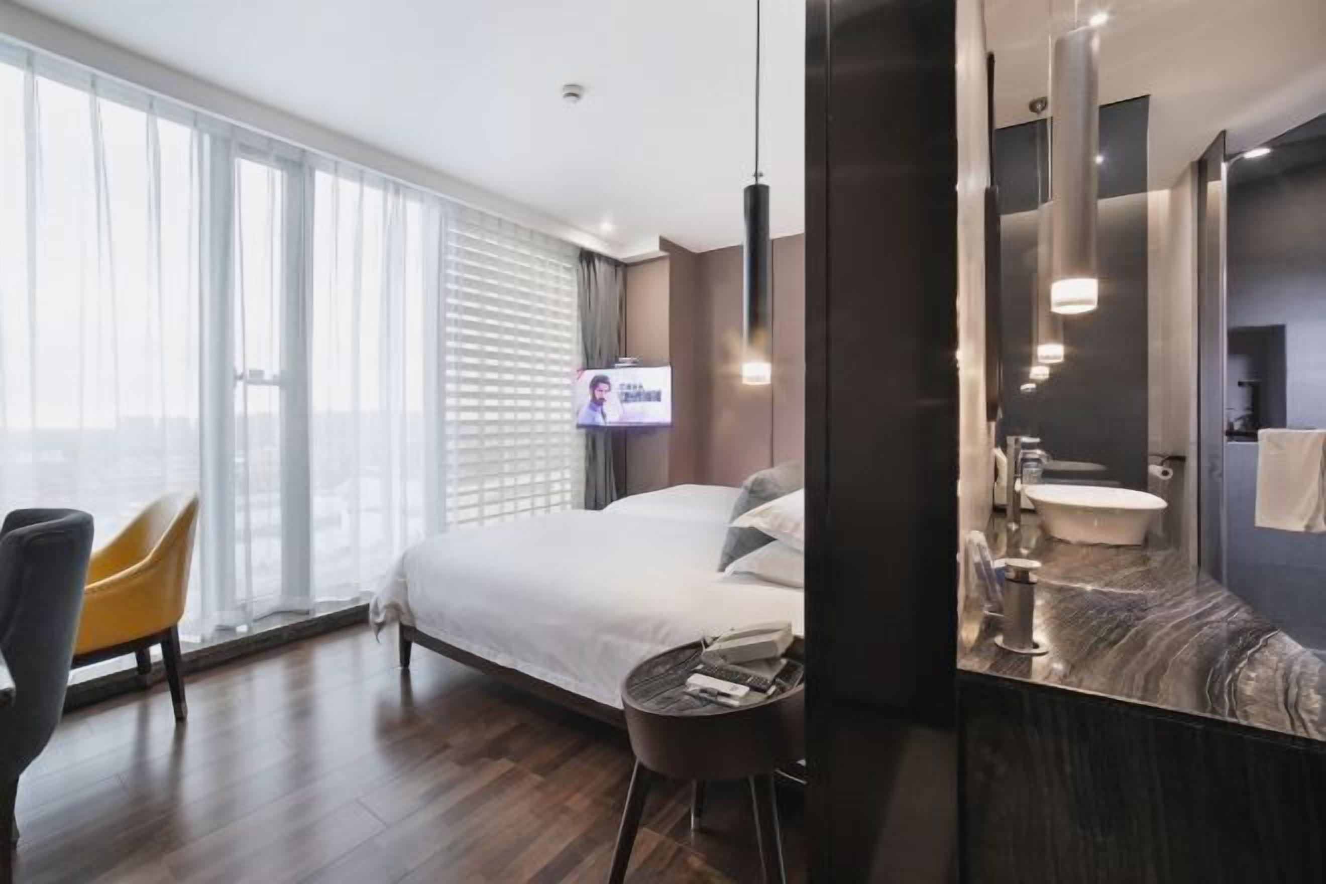 Quarto de hotel com uma cama, uma mesa redonda, uma cadeira, um espelho grande, uma pia e uma televisão.