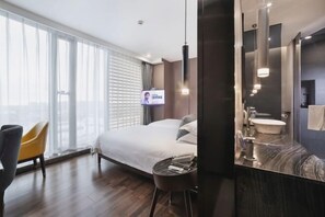A hotel room with a bed, a round table, a chair, a large mirror, a sink, and a television. - Puyuan X Hotel (Tongxiang)