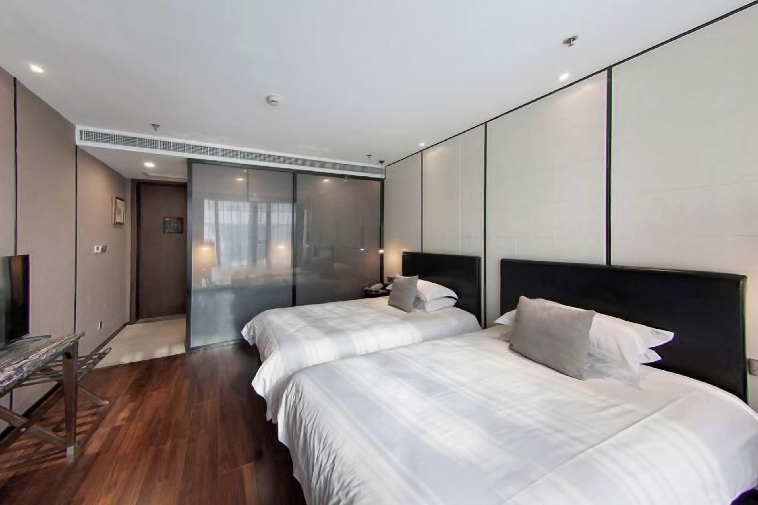 A modern hotel room with two beds, a wooden floor, a glass partition, and a flat-screen TV.