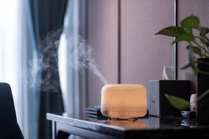 Una habitación moderna con un diseño elegante y minimalista, que incluye un difusor de aromas sobre una mesa de madera, una planta en maceta y un espejo que refleja el interior de la habitación.