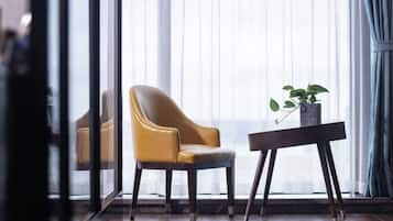 Una habitación con un ventanal grande, una silla amarilla, una mesita con una planta y suelo de madera.