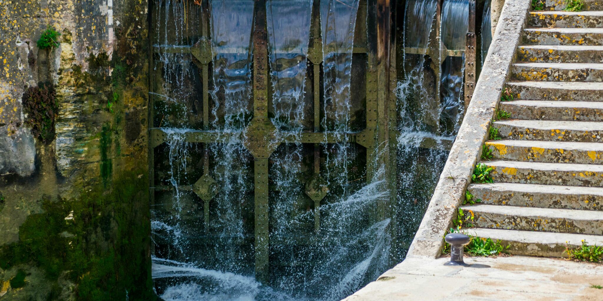 Een stenen trap die leidt naar een waterpartij met een metalen constructie.