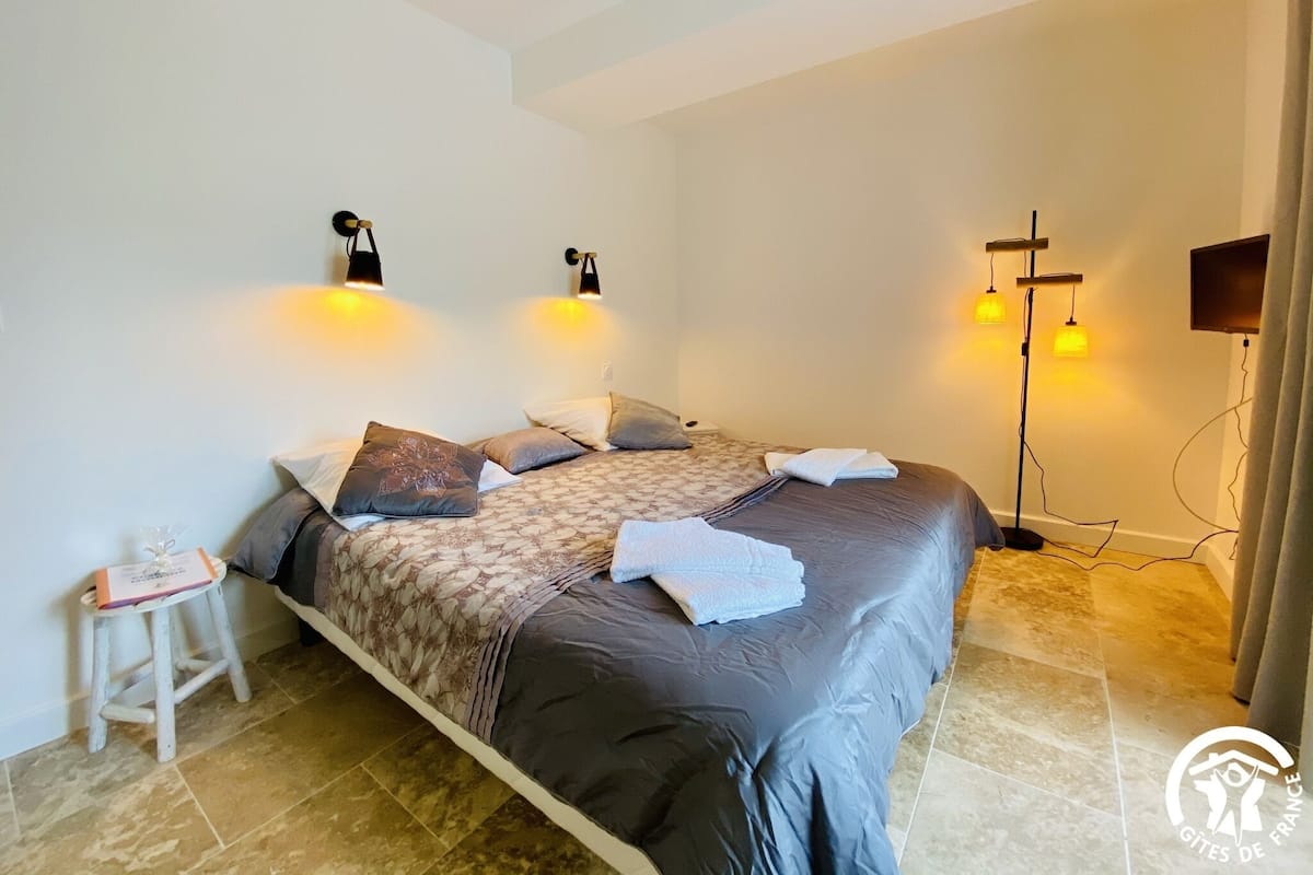 Une chambre à coucher avec un lit, deux lampes fixées au mur, une télévision et un petit tabouret.