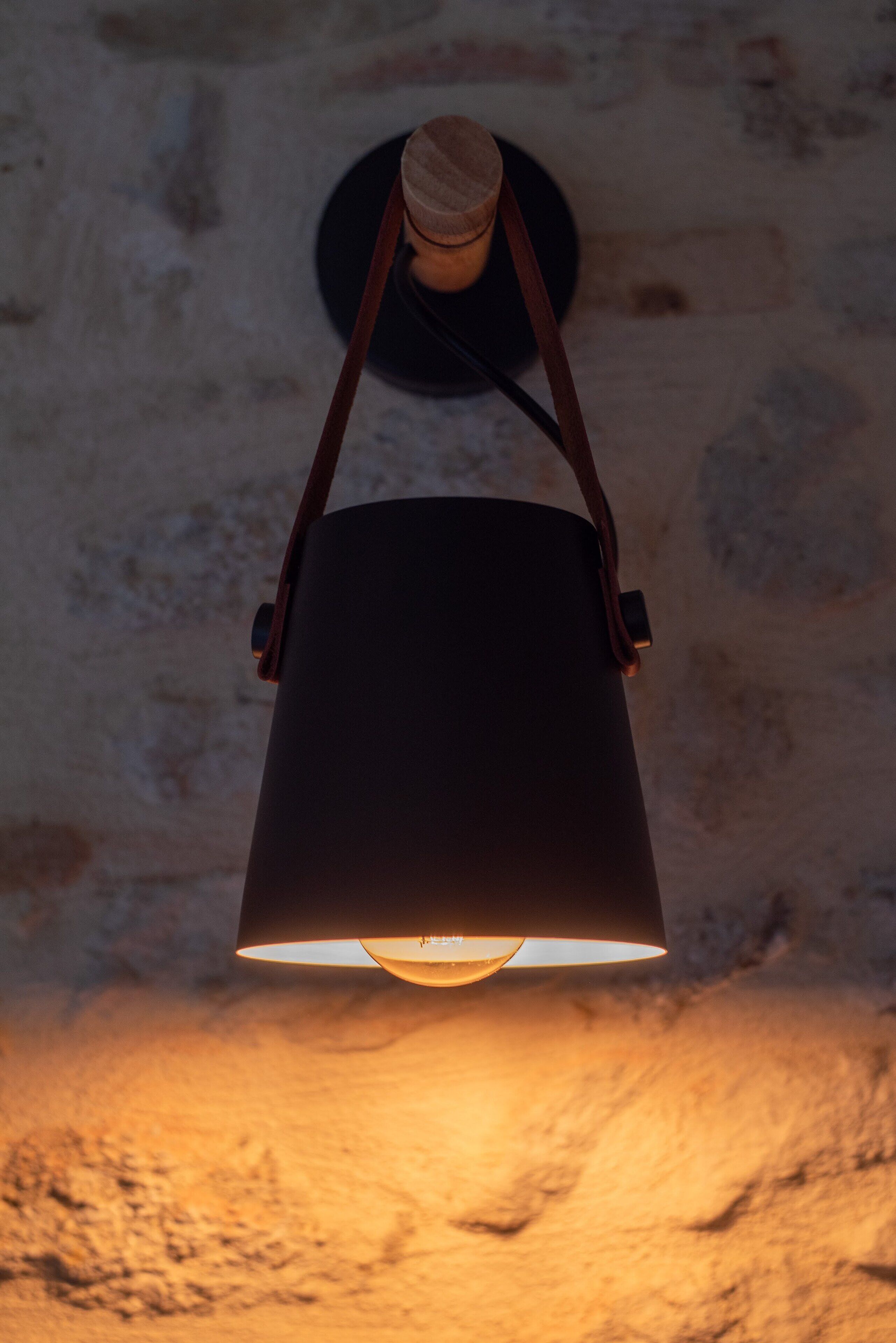 A hanging lamp with a wooden handle and a black shade, mounted on a textured wall.