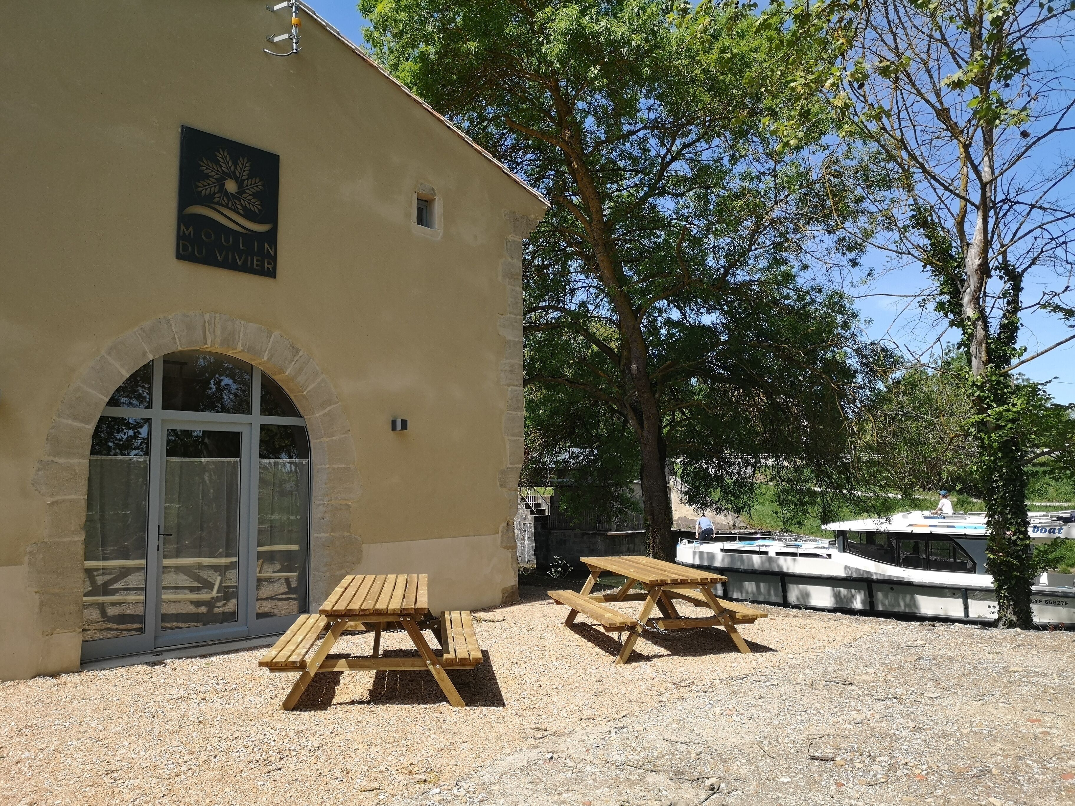 A building with a sign reading "Moulin du Vivier" and two wooden picnic tables outside.