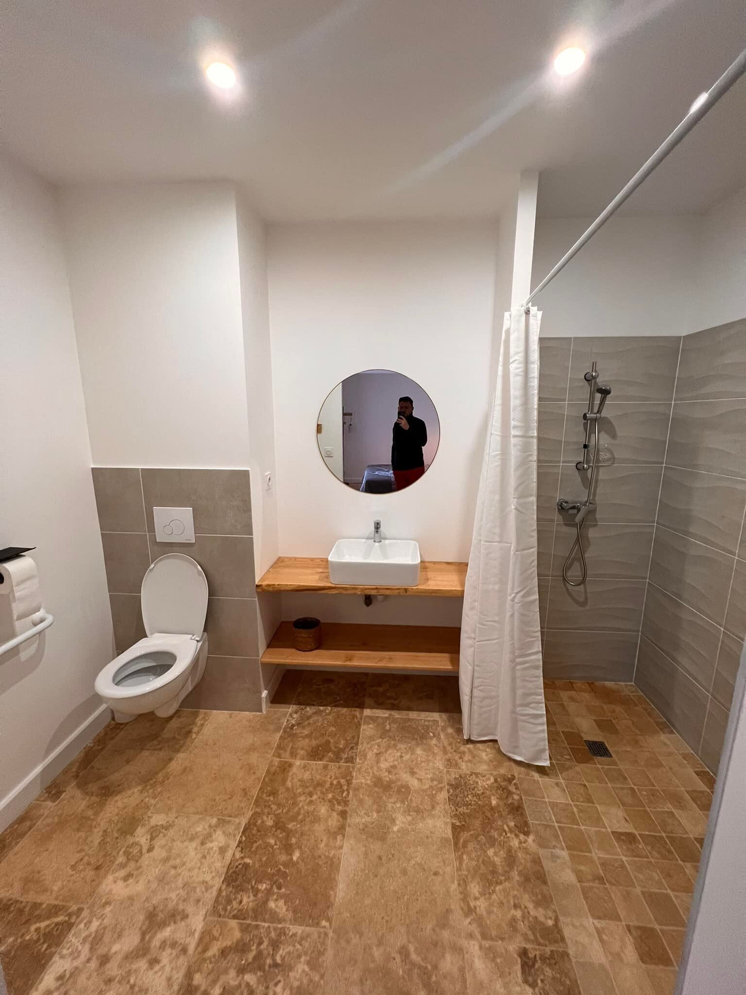 Une salle de bain comprenant des toilettes, un lavabo, un miroir, une douche et un porte-serviettes.
