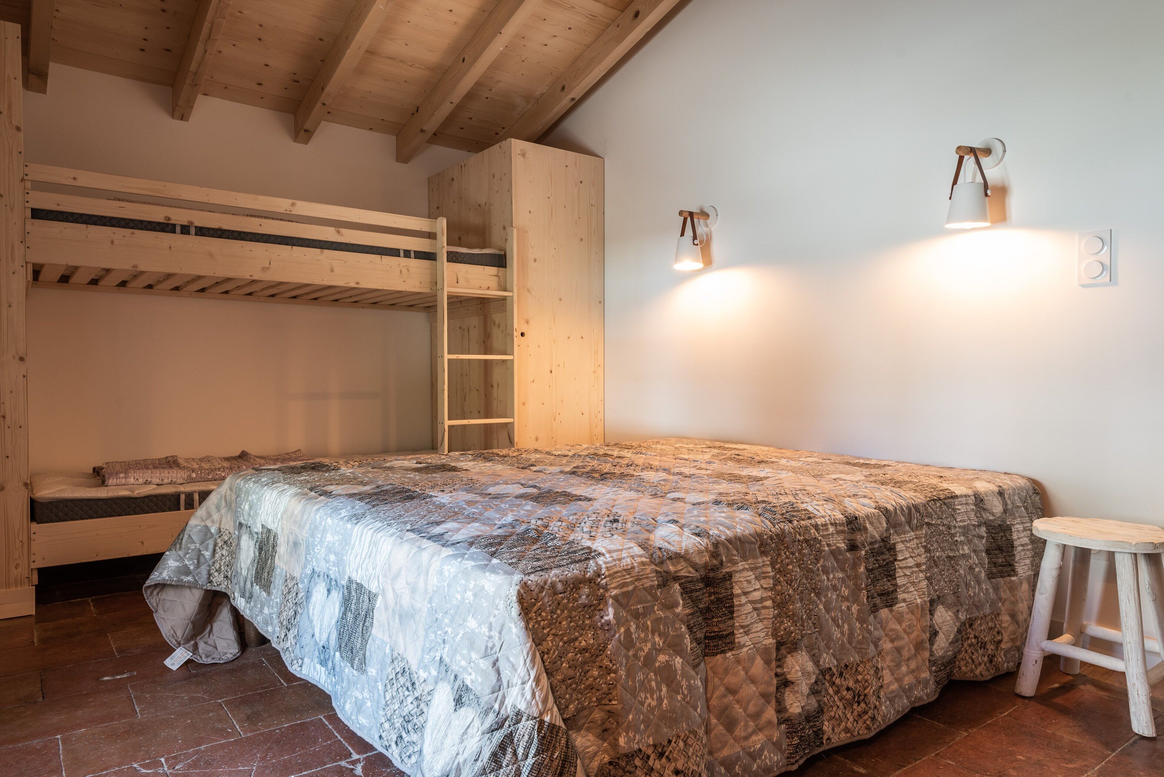 Un lit superposé avec une courtepointe matelassée, une échelle en bois et un petit tabouret.