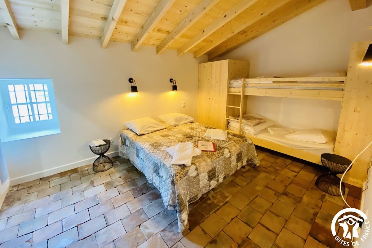 Une pièce avec un lit, un lit superposé, une fenêtre et un sol en briques.