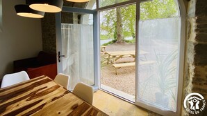 Een eetgedeelte met een houten tafel en stoelen, een stenen muur en een groot rondboogvenster met uitzicht op een terras.