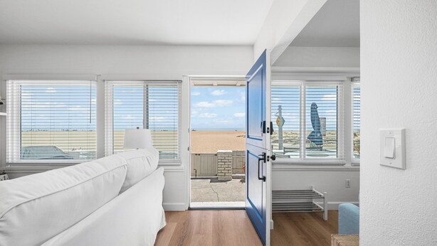A room with a white sofa, a wooden floor, and a view of the beach through a door. - Charming 2 Story/4 Bedroom Home on the Boardwalk (Newport Beach)