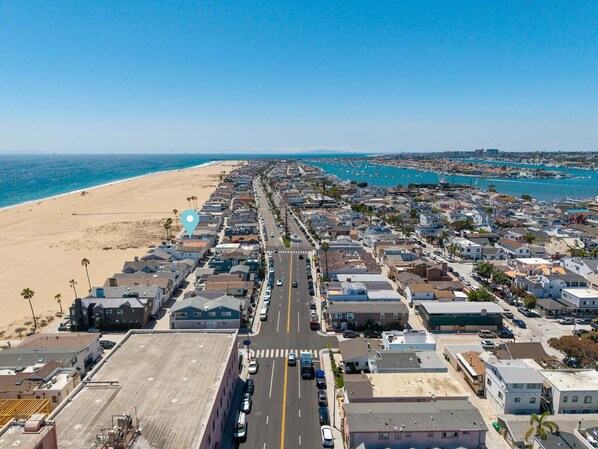 Un pueblo costero con playa, una larga calle bordeada de casas y un puerto deportivo con barcos.