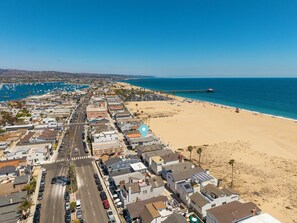 An aerial view of a coastal town with a beach, a pier, and a road leading to the beach.