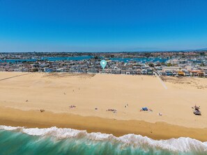 Vista aérea de una playa con casas, cielo despejado y olas.