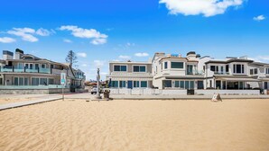 Una propiedad frente a la playa con una playa de arena, una calle con casas y un cielo azul despejado.
