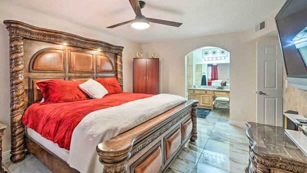 Een slaapkamer met een groot houten bed, een plafondventilator en een badkamer in de achtergrond.