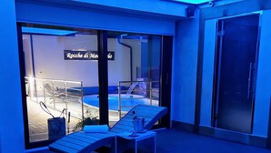 A modern outdoor area with a wooden deck, a hot tub, and a glass door leading to a pool area.