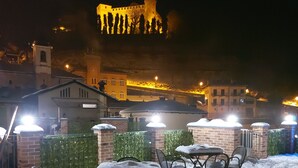 An outdoor seating area covered in snow with tables and chairs, overlooking a historic building with a tower at night.