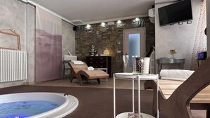A modern room with a stone wall, a wooden bench, a small table with a glass, and a hot tub.