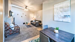 A modern living room with a dark wood dining table, a patterned sofa, a ceiling fan, and a sailboat painting on the wall. - Apartment w/ Patio & Grill Access ~ 1/2 Mi to Bay! (Anacortes)
