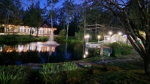 Een lodge aan het meer met een steiger, een fontein en een verlicht gebouw.