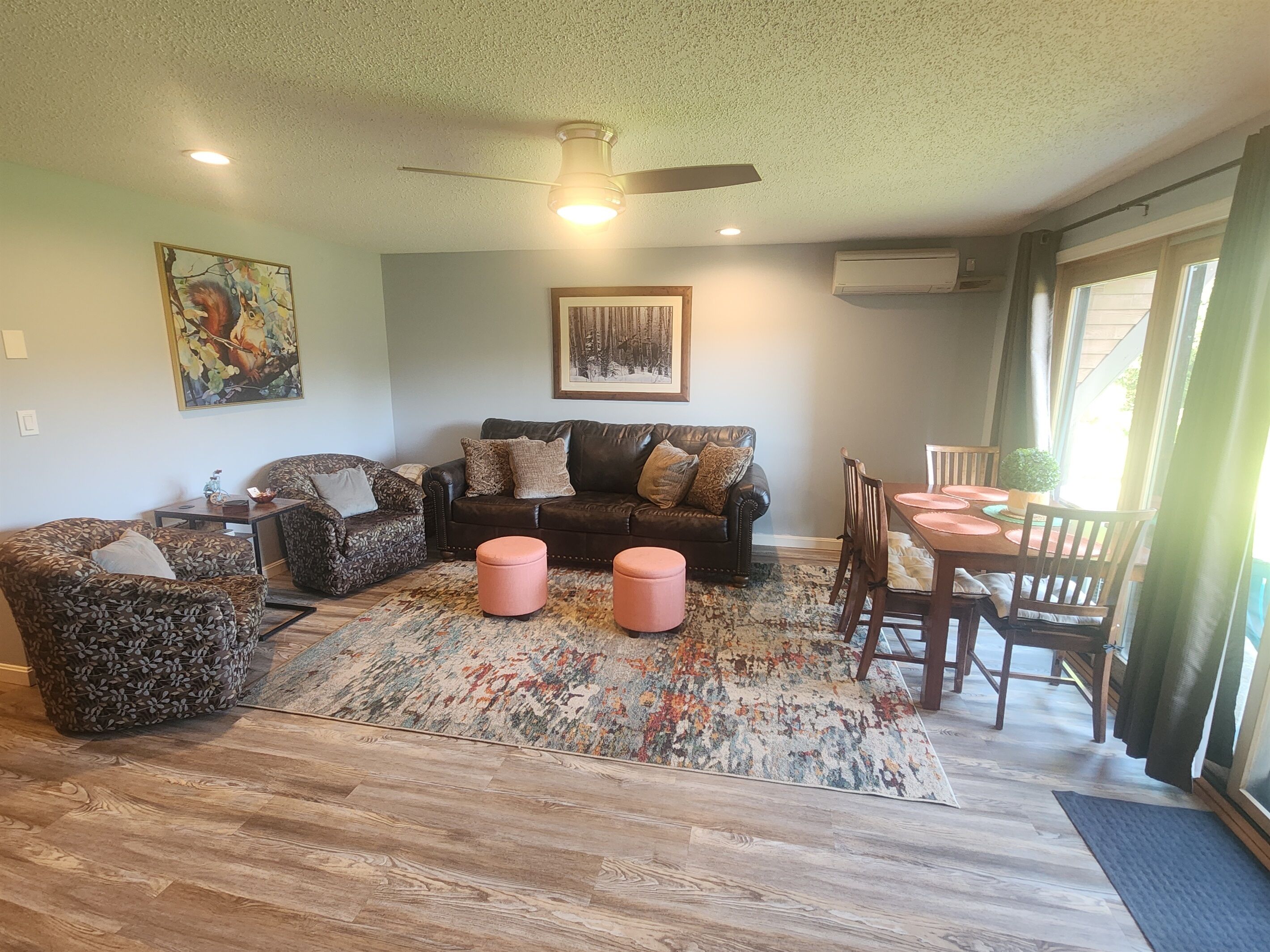 Ein Wohnzimmer mit einem dunkel-ledernen Sofa, gemusterten Sesseln, einem Couchtisch und einem Essbereich mit Tisch und Stühlen.
