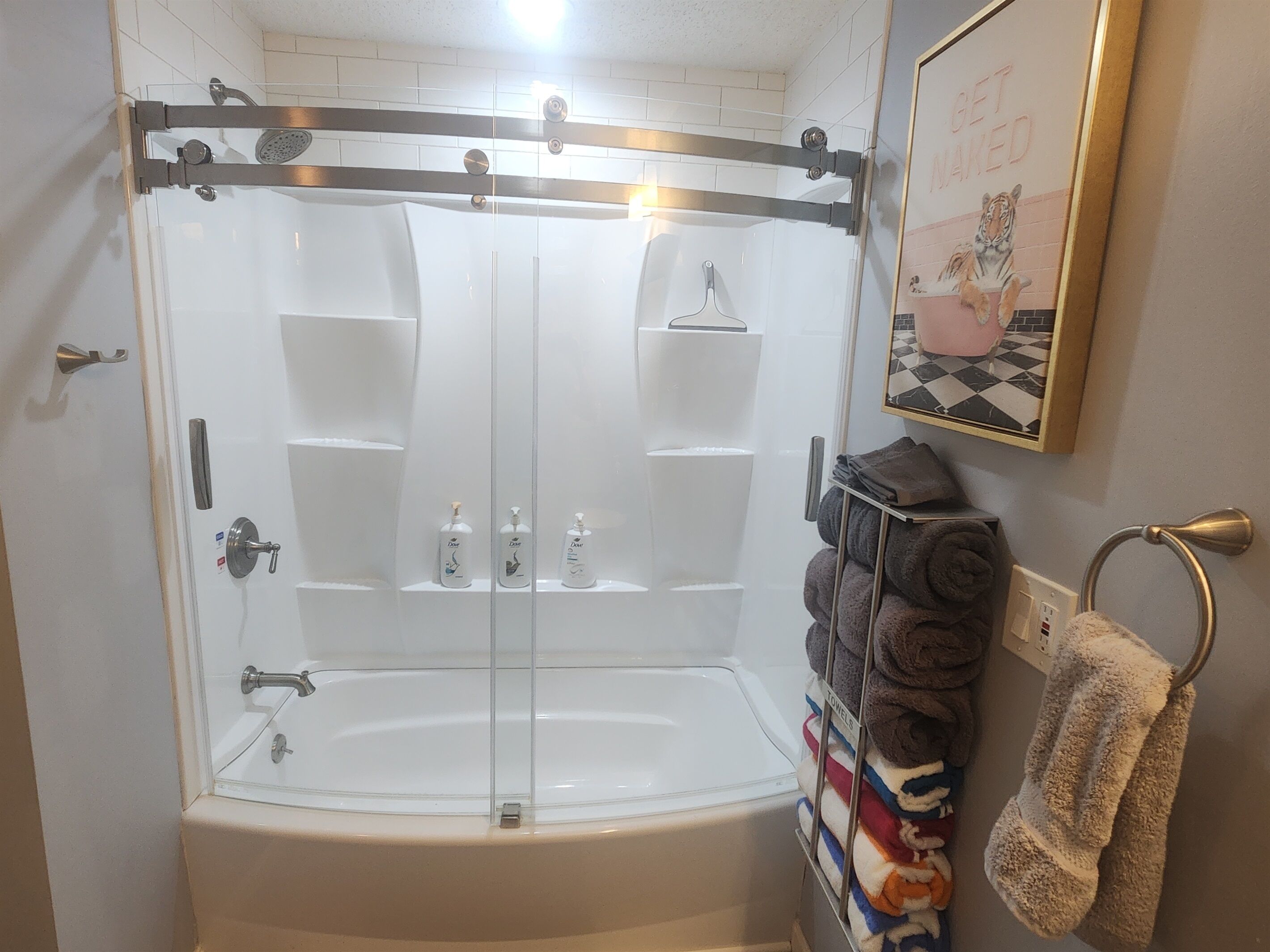 A walk-in shower with a glass door, a towel rack with towels, and a framed picture on the wall.