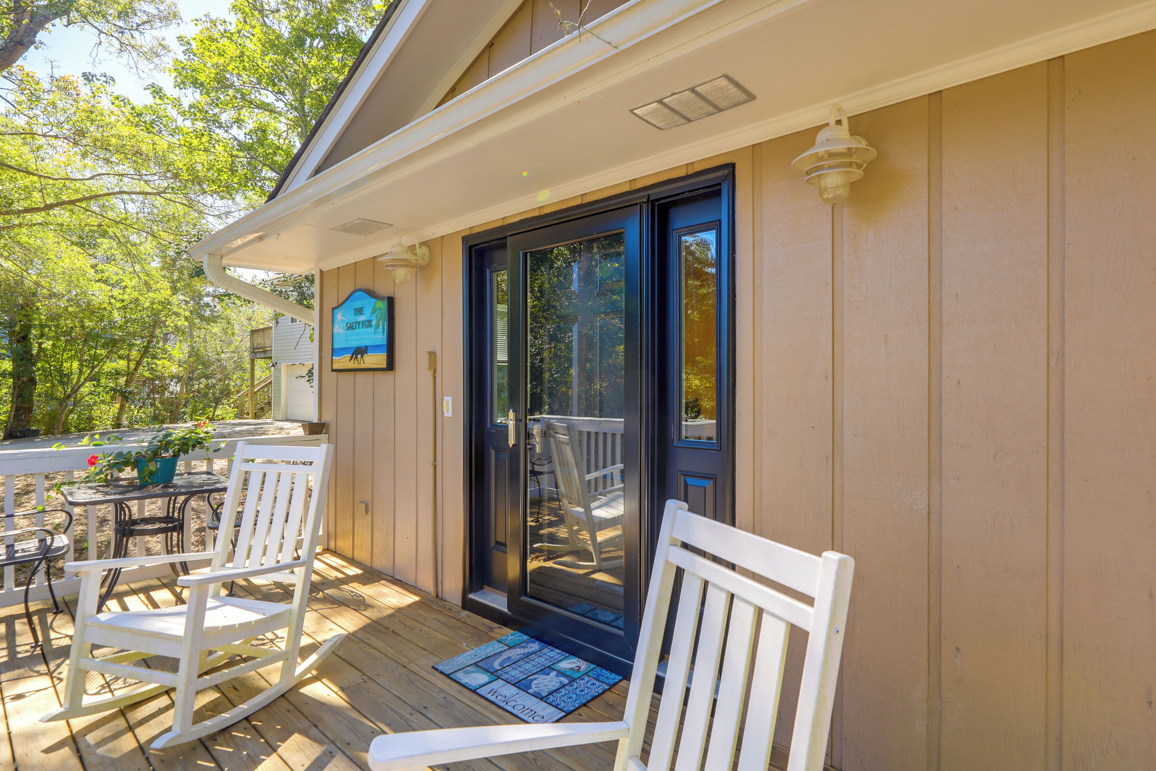 Une terrasse en bois avec des fauteuils à bascule blancs et un paillasson.