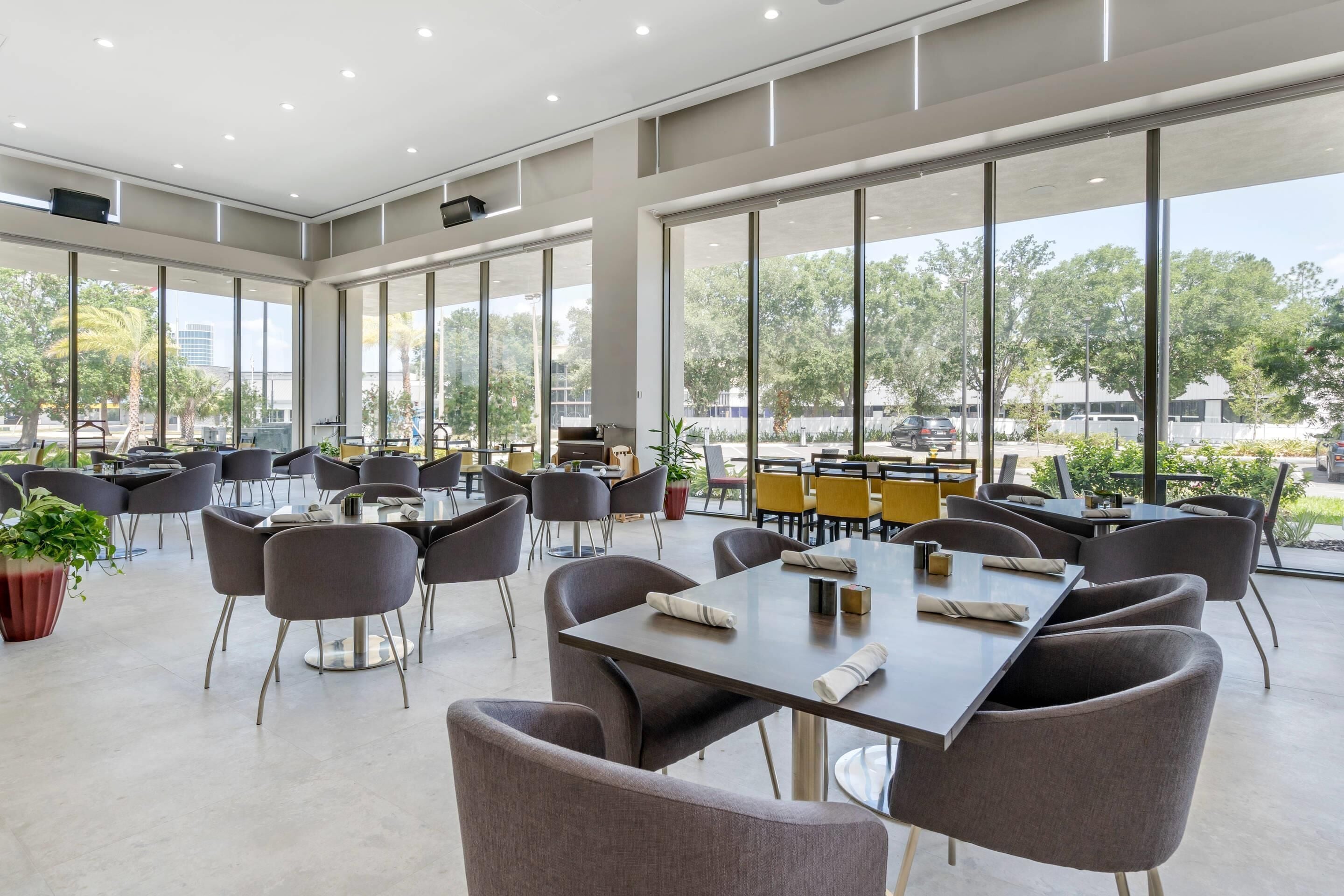 A spacious indoor dining area with large windows, modern furniture, and a view of the outdoors.