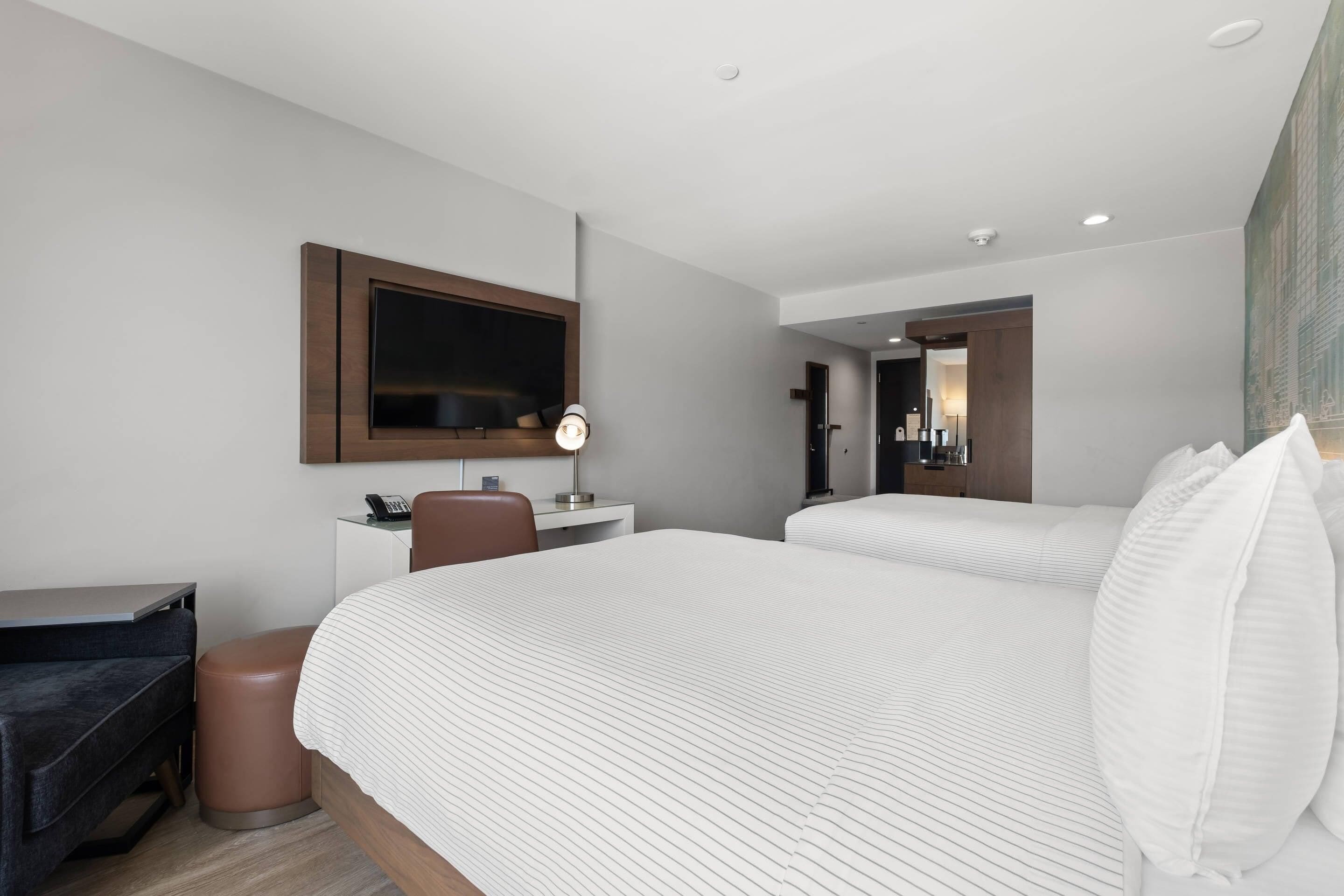 A hotel room with two beds, a desk, a chair, a TV, and a trash bin.