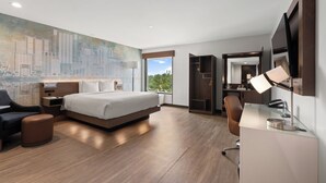 Una habitación de hotel moderna con una cama grande, un escritorio con lámpara, una silla, un armario y un mural con vista a la ciudad.