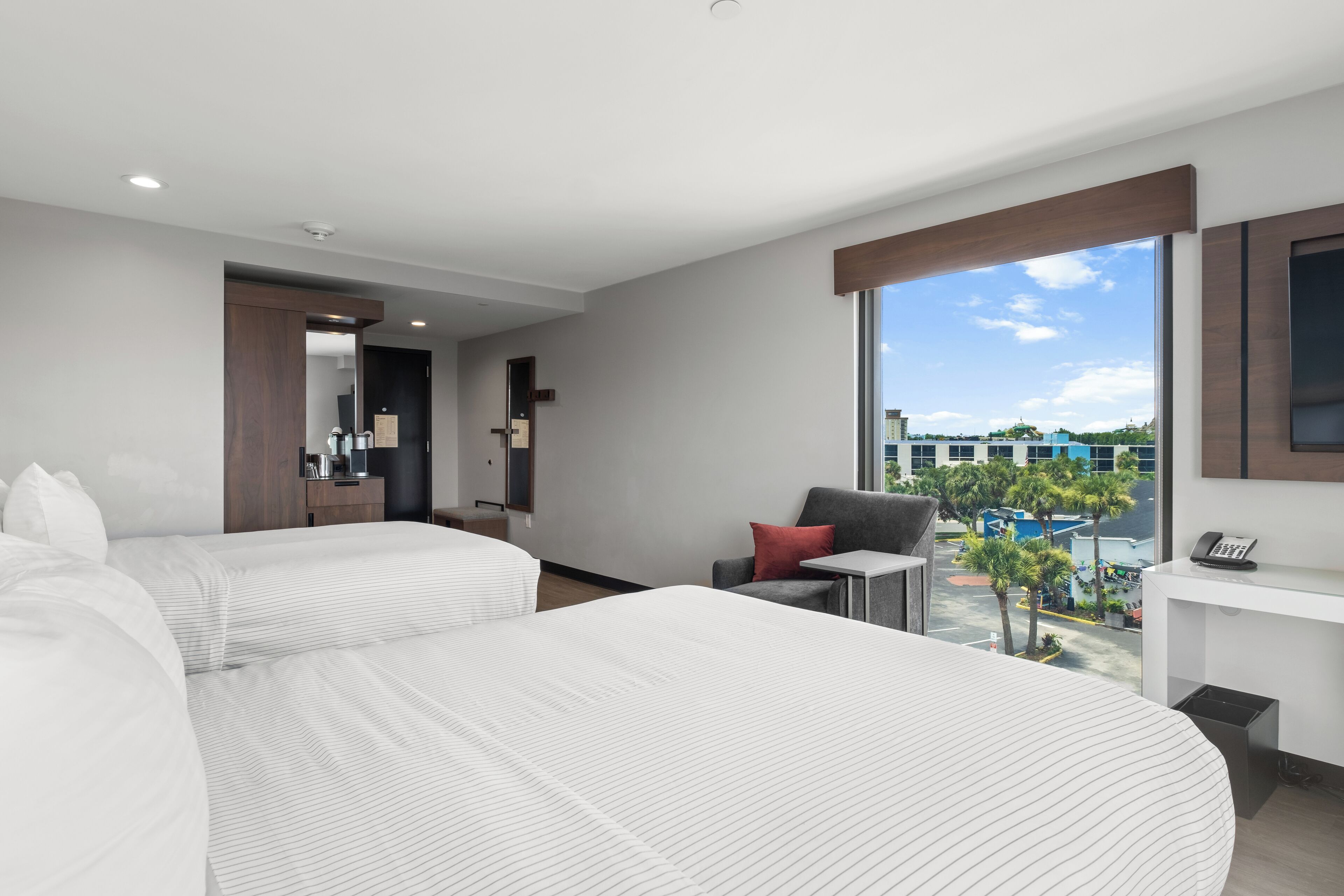 Une chambre d’hôtel moderne dotée de deux lits, d’un petit coin salon, d’un bureau et d’une grande fenêtre donnant sur la ville.