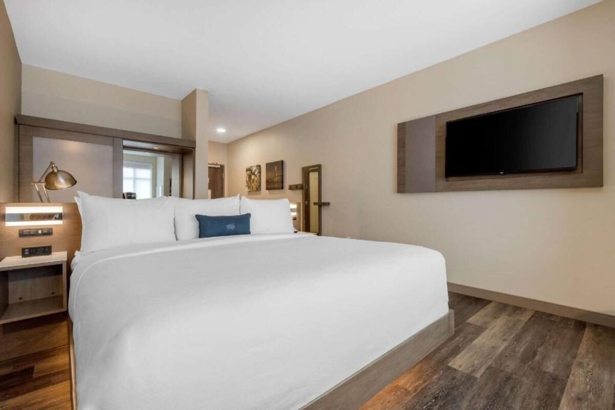 Habitación de hotel con una cama grande, un televisor de pantalla plana en la pared, una mesita de noche con lámpara y suelo de madera.