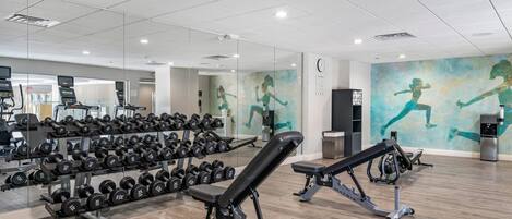 Academia com equipamentos de ginástica, um relógio e um mural de um corredor.