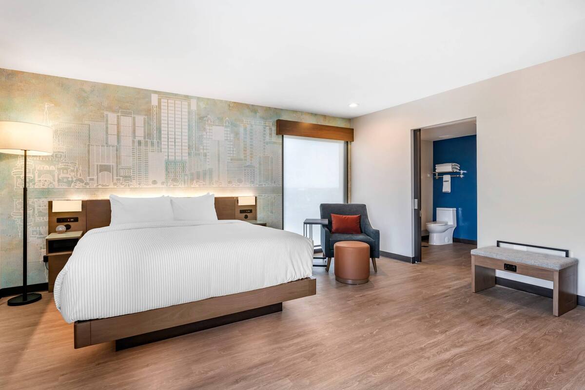 Habitación de hotel moderna con una cama grande, un mural con vista a la ciudad, un escritorio, una silla y una mesita.