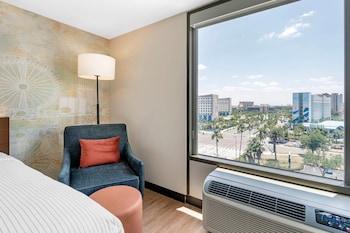 A modern hotel with a glass facade, outdoor seating area, and a parking lot. at Cambria Hotel Orlando Universal Blvd