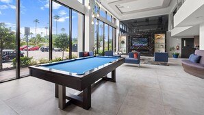 Una mesa de billar en un espacio interior moderno con ventanas amplias, una zona de estar y un televisor.